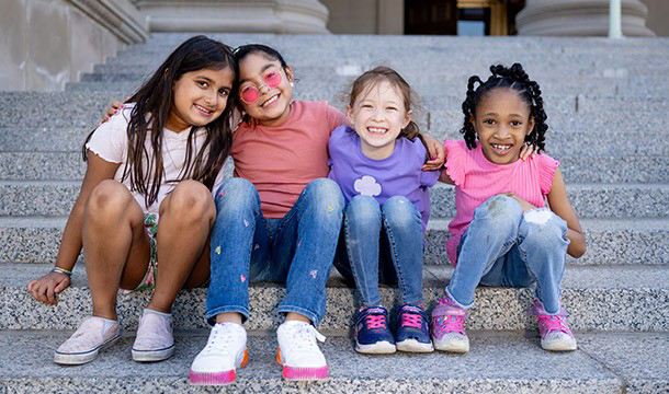 A volunteer is pictured with three Girl Scouts--one wearing a Brownie sash, one wearing a Daisy vest, and another wearing a Junior sash.